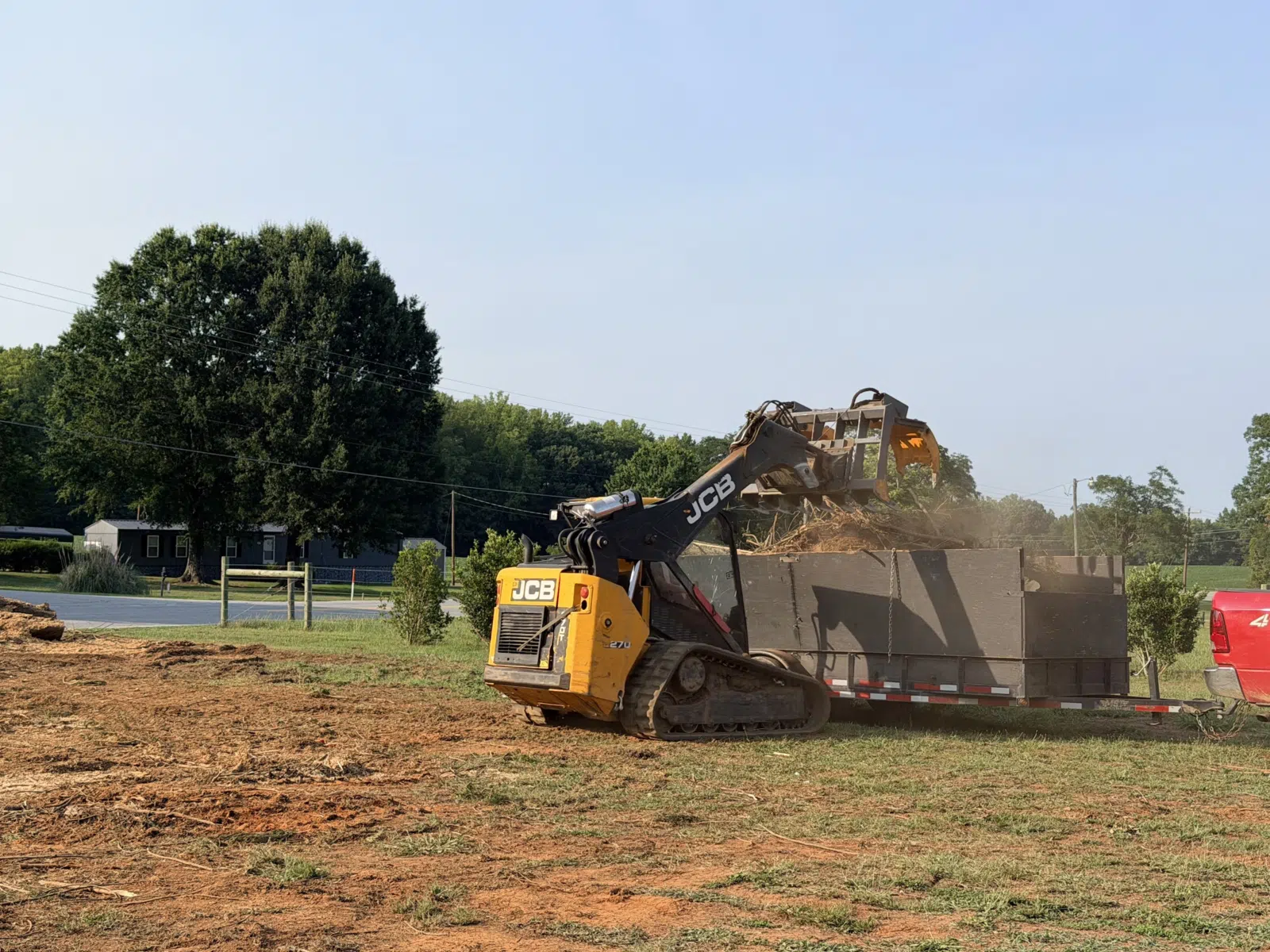 JCB skid steer dumping brush into a trailer in a field — Your Way Lawn and Tree in Greensboro